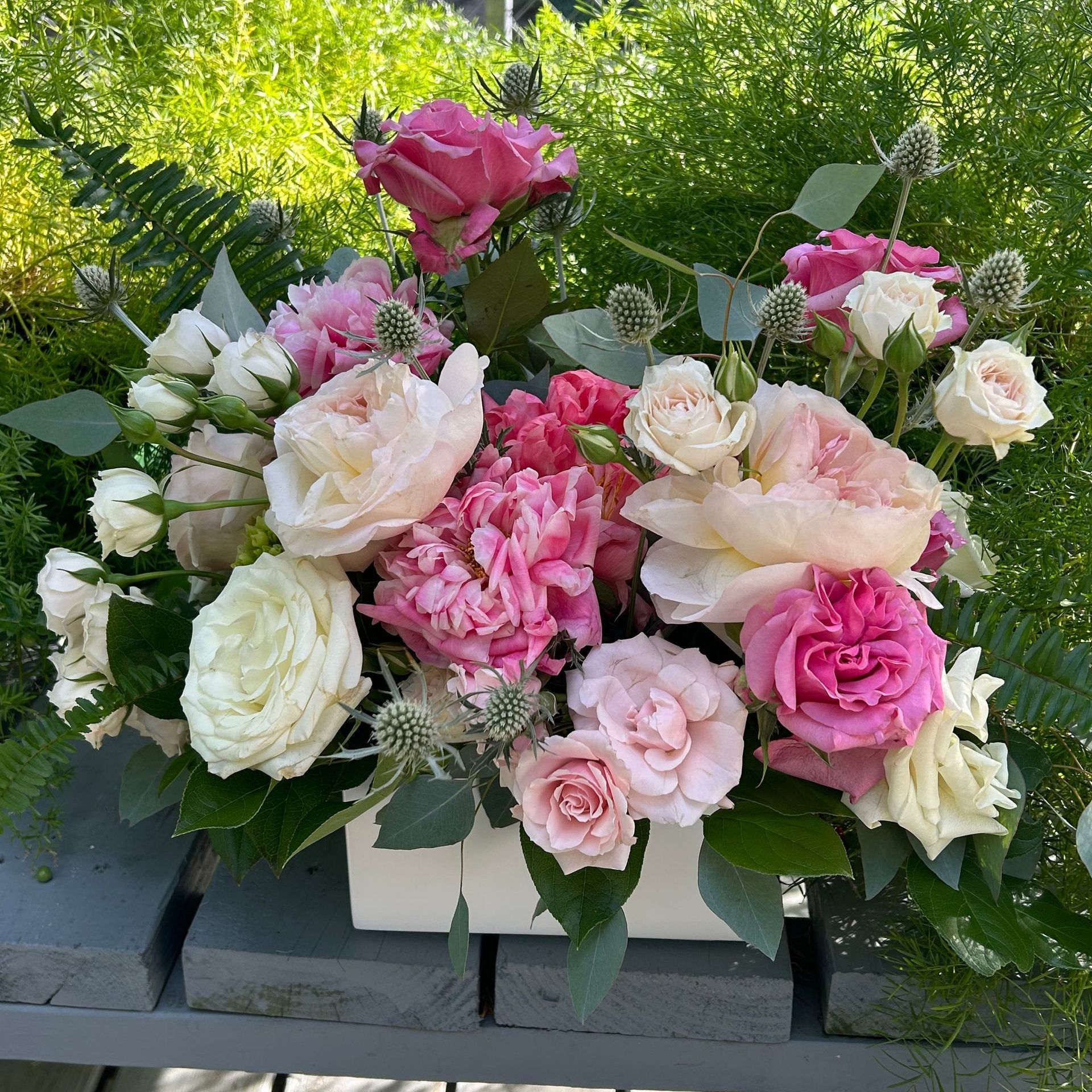 A white box filled with pink and white flowers is sitting on a wooden table.
