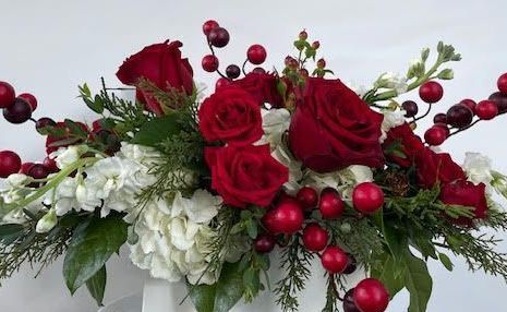 A centerpiece filled with red and white flowers with greenery sits on a table for Christmas holiday