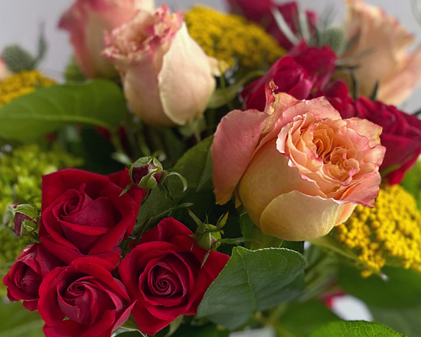Close-up of a mixed bouquet of roses in shades of red and peach, with green foliage and yellow accents.