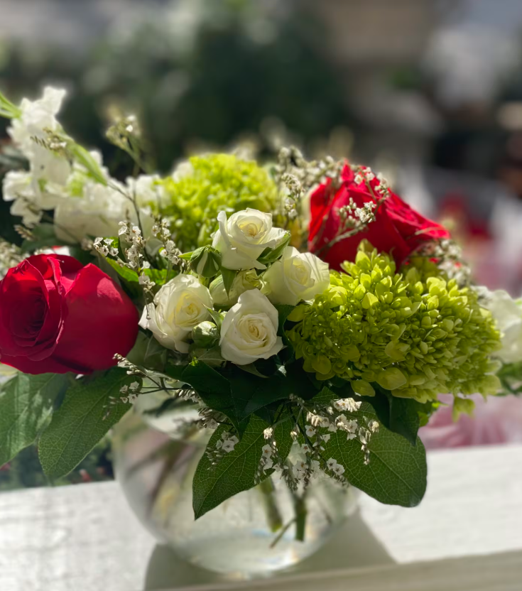 Bouquet of red roses, white roses, and green flowers in a clear glass bowl.