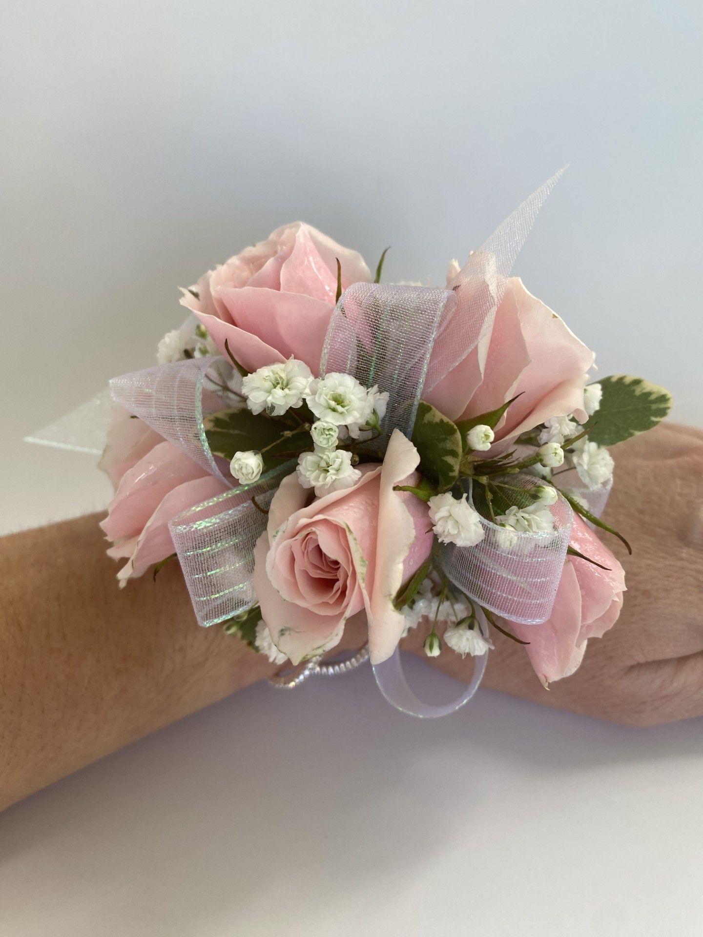 A woman is wearing a wrist corsage of pink roses and baby's breath.
