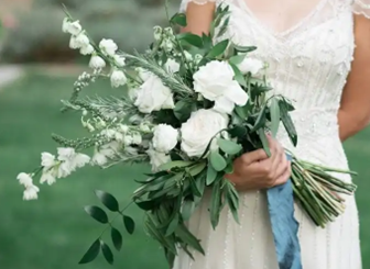 Bride holding a white floral bouquet with greenery; blue ribbon.