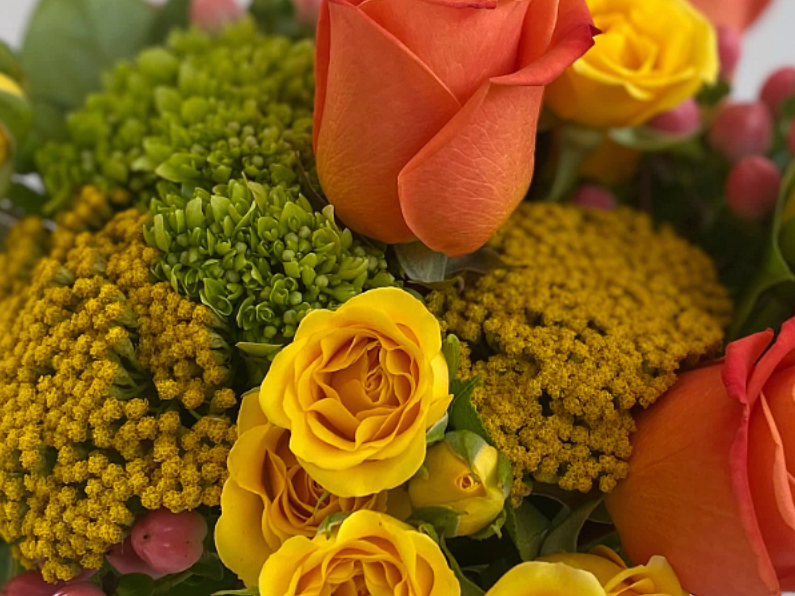 Close-up of a bouquet with yellow, pink, and white flowers, including roses and small pink blossoms.