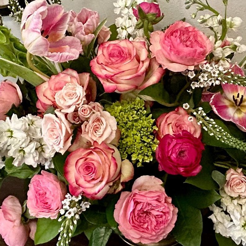 Close-up of a floral arrangement with pink roses, tulips, and small white flowers.