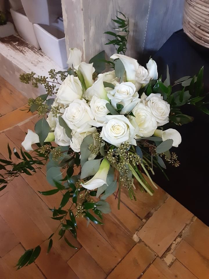 White rose and calla lily bouquet with greenery on a wooden surface.