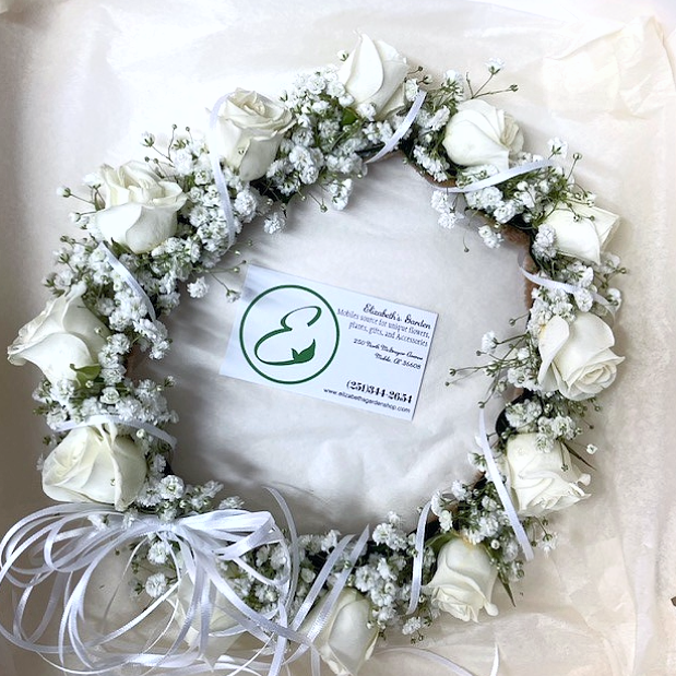 White rose and baby's breath flower crown. The crown sits on white tissue paper with a business tag.