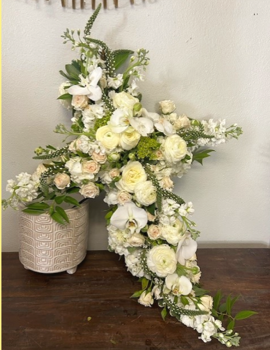 Floral arrangement in the shape of a cross, white and cream flowers, pot on a wooden table.