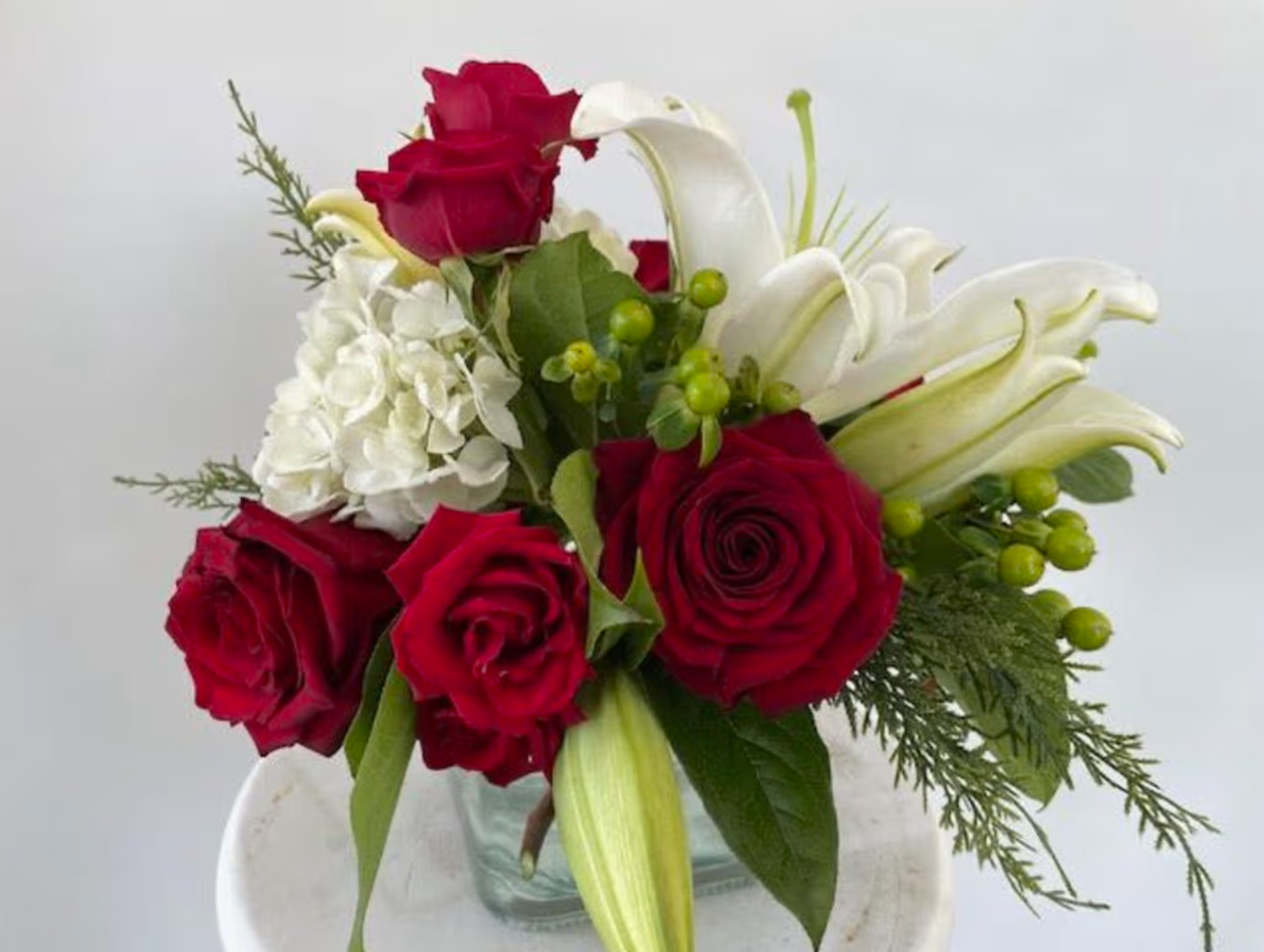 Red roses and white lilies in a glass vase, arranged with greenery.