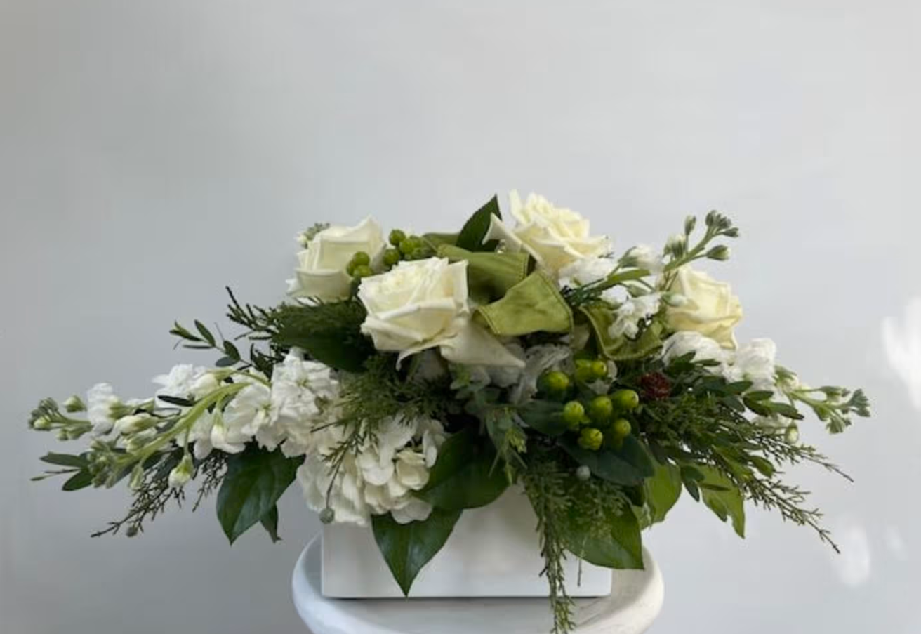 White floral arrangement with roses and greenery in a white container.