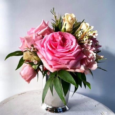 A silver vase filled with pink and cream roses sits on a table