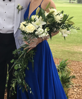 Woman in blue gown holding a white floral bouquet; man in tuxedo beside her.