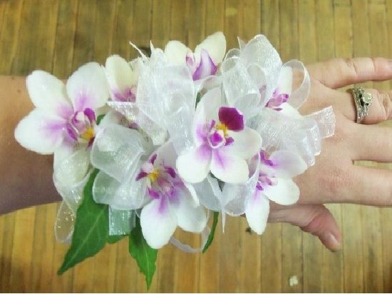 White and purple orchid wrist corsage with white ribbon on a hand.