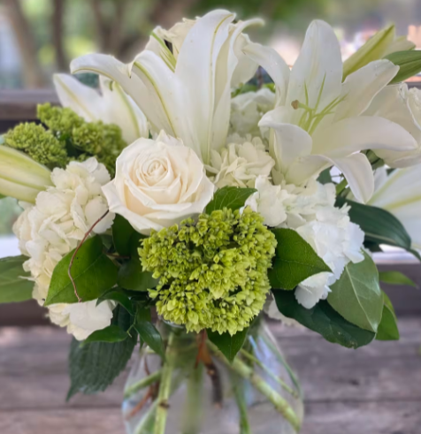 A vase filled with white flowers and greenery on a table.