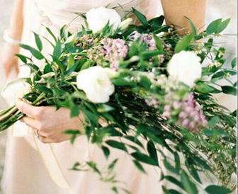 Bride holding a bouquet of white roses, lavender buds, and green leaves; neutral dress.