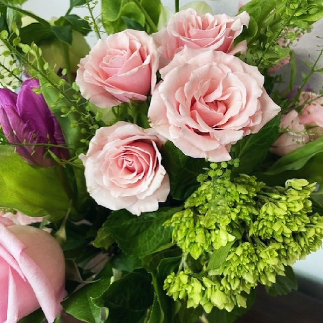 Pink roses and green foliage in a flower arrangement.