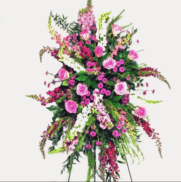 Floral arrangement of pink roses and other flowers on a stand.
