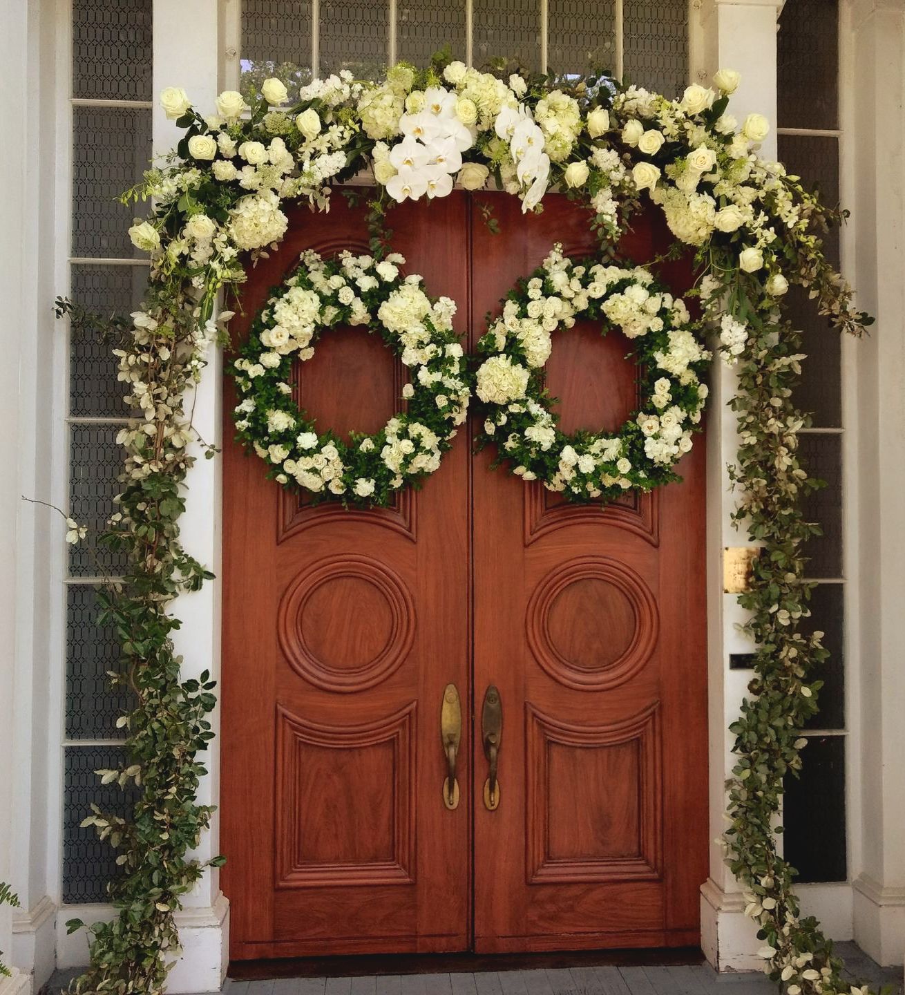 Wooden double doors decorated with white floral wreaths and garland.