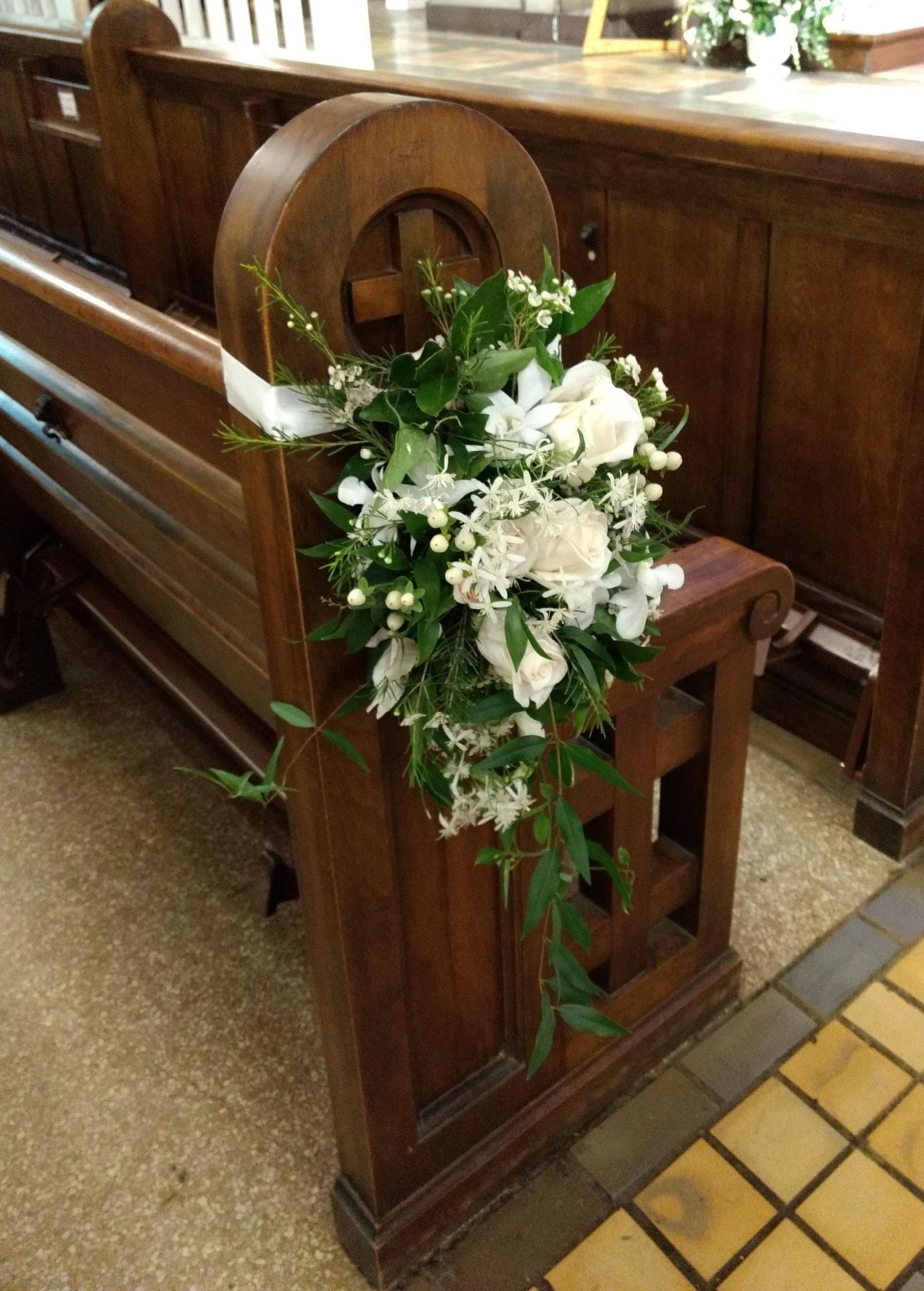 Flower arrangement on a wooden church pew, decorated with white flowers and greenery.