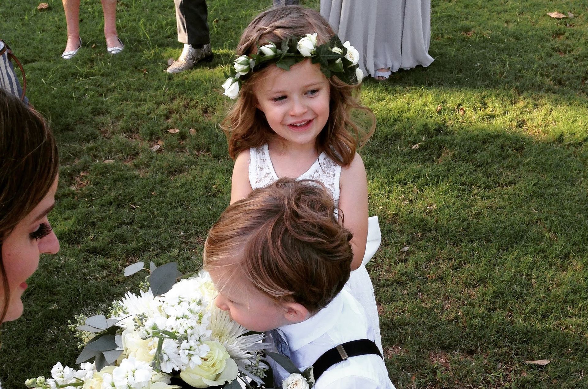 A little girl wearing a flower crown is sitting next to a boy holding a bouquet of flowers.