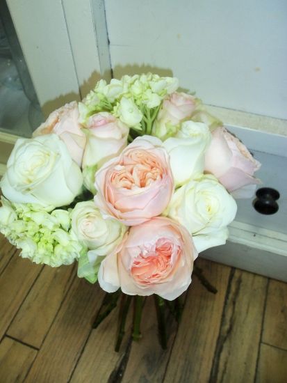Bouquet of pale pink and white roses and green hydrangeas on wooden floor.