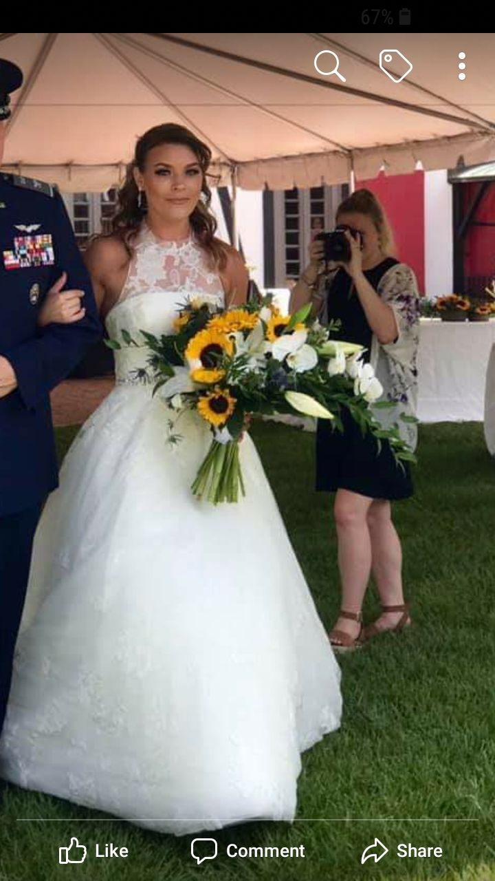 Bride in white dress holding sunflowers, being photographed at outdoor wedding.
