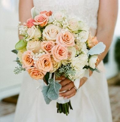 Bride holding a bouquet of peach and cream roses, wearing a white dress.