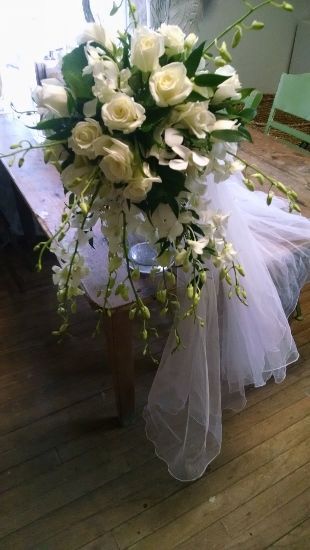 White roses and orchids cascade over a white draped table; wood floor.
