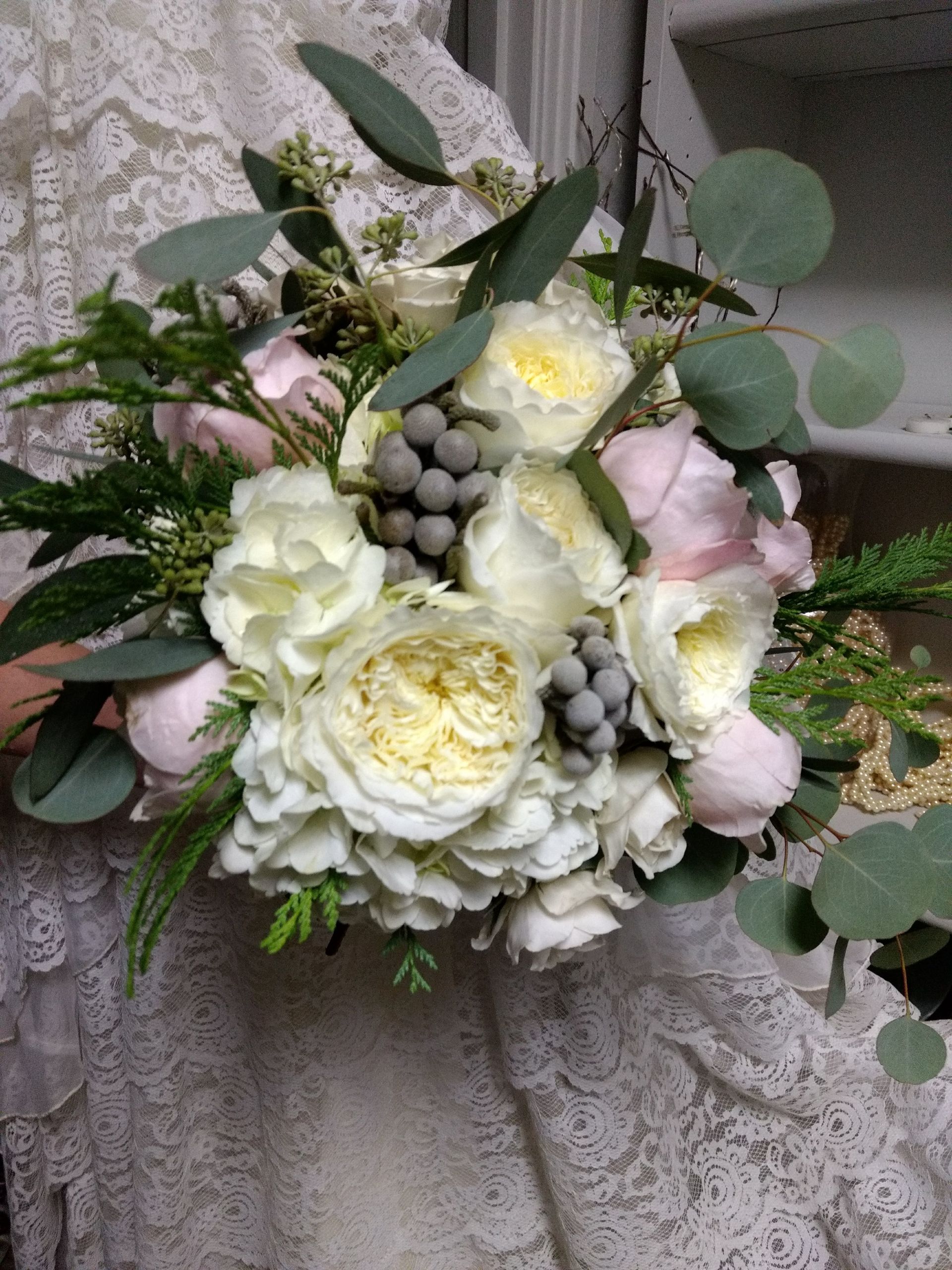 Wedding bouquet with white and pink flowers, gray berries, and green foliage held by a person.