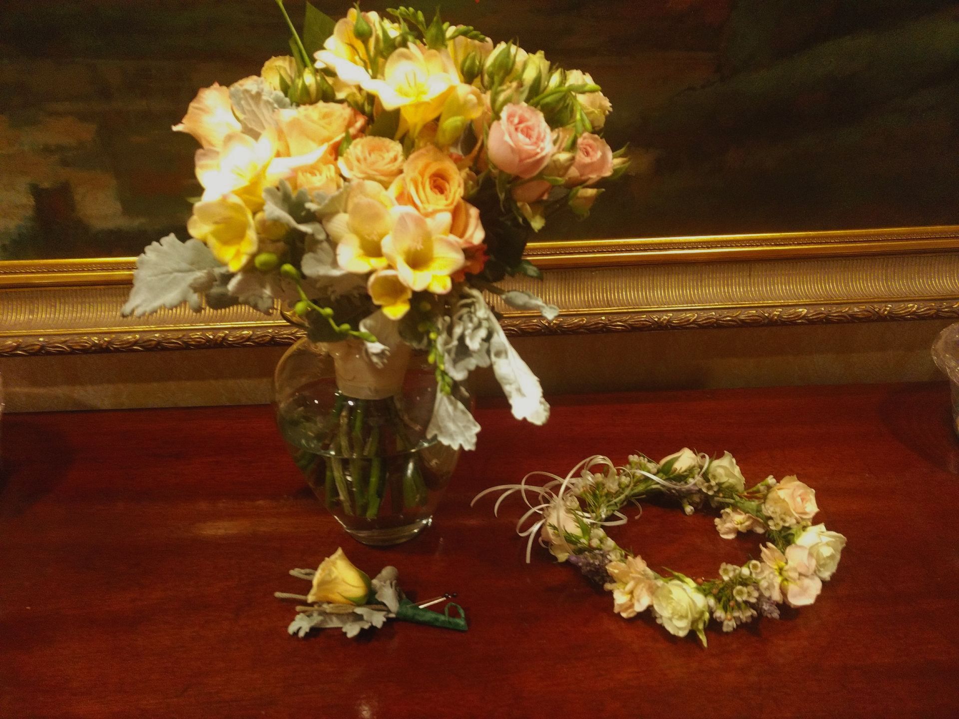Bouquet of yellow and pink flowers, with a wreath and boutonniere on a wood table.