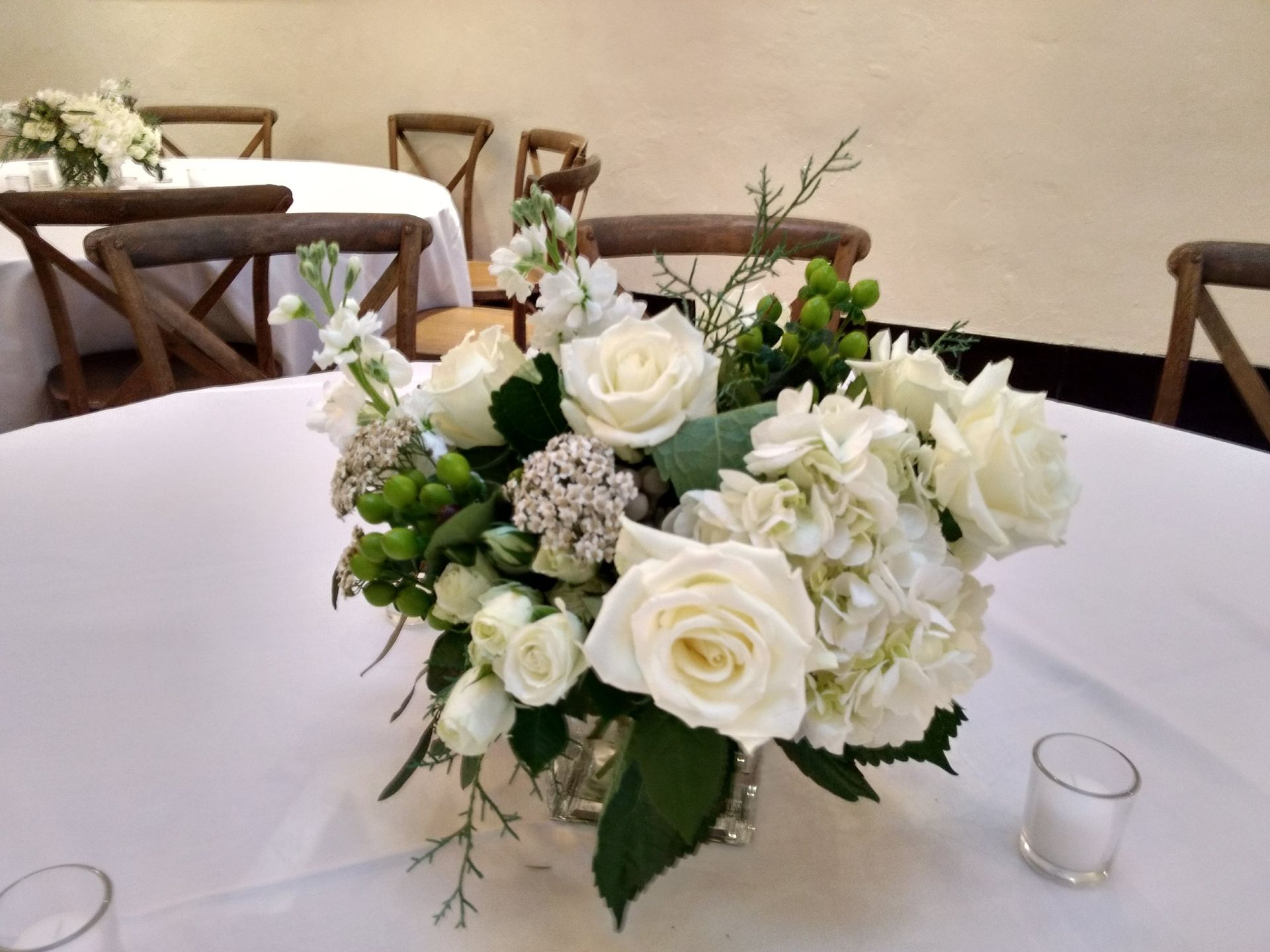 Centerpiece of white roses, hydrangeas, and greenery on a table with white tablecloth.