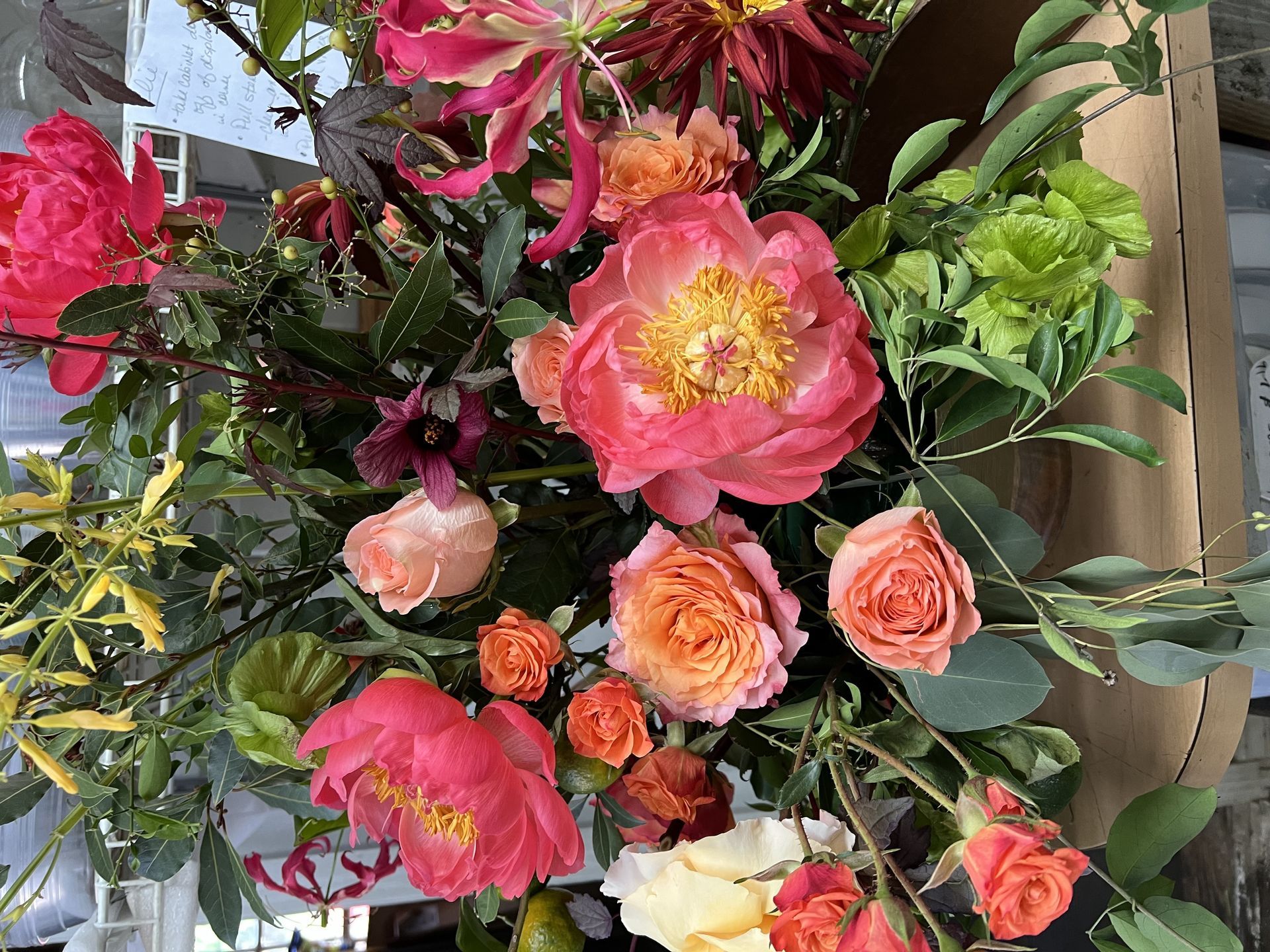 A vibrant floral arrangement with pink and orange peonies, roses, and greenery.