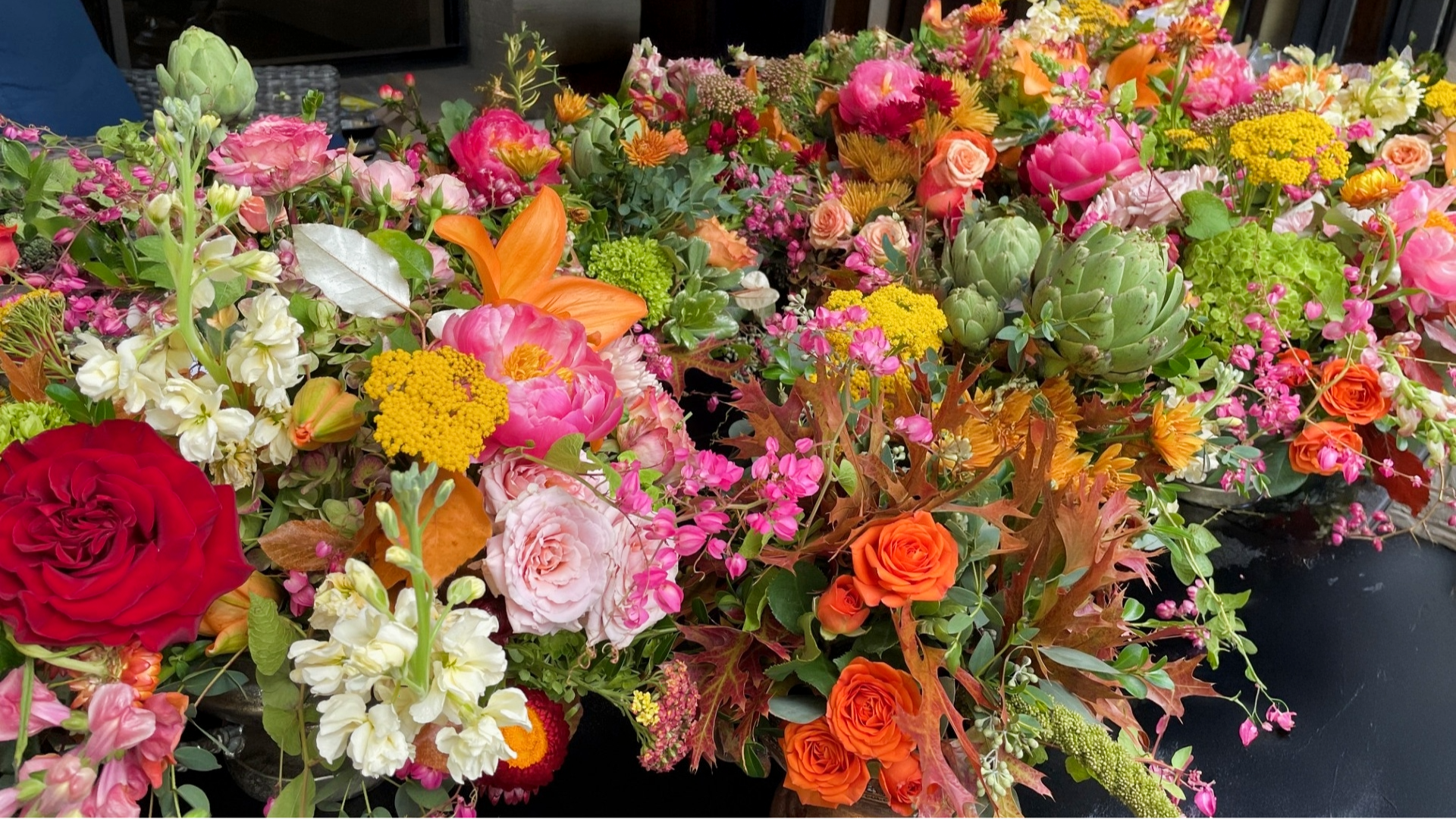 Floral arrangement with orange flowers, moss spheres, birch logs, and decorative accents, on a light background.