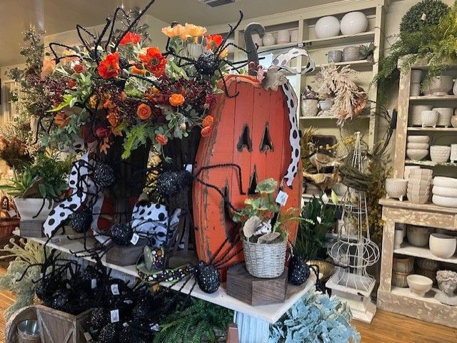 An orange wooden pumpkin stands next to floral arrangements and spiders.