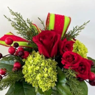 Floral arrangement in a glass square vase, featuring red roses, green hydrangeas, berries, and a red and green bow.