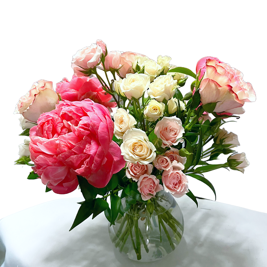 A glass vase filled with pink peonies, roses, and tiny pink and white roses.