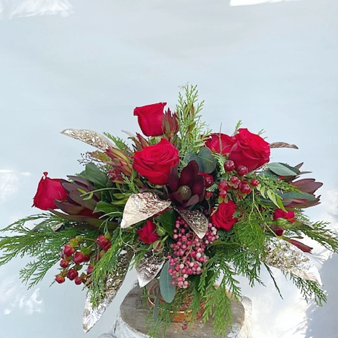 Red roses in a holiday floral arrangement, with greenery, berries, and metallic accents.