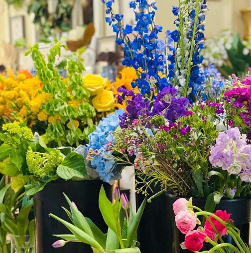 Colorful flower display: yellow, blue, purple, and pink blossoms in black vases.