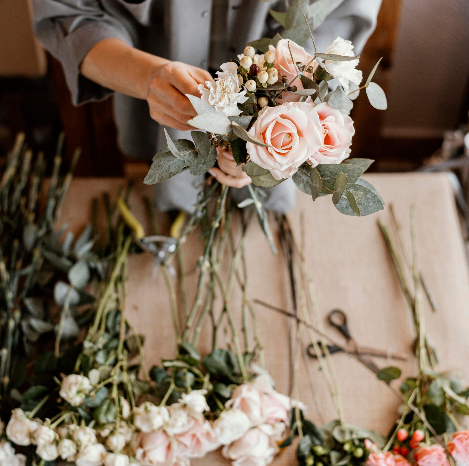 Person arranging a bouquet of roses and greenery on a table.
