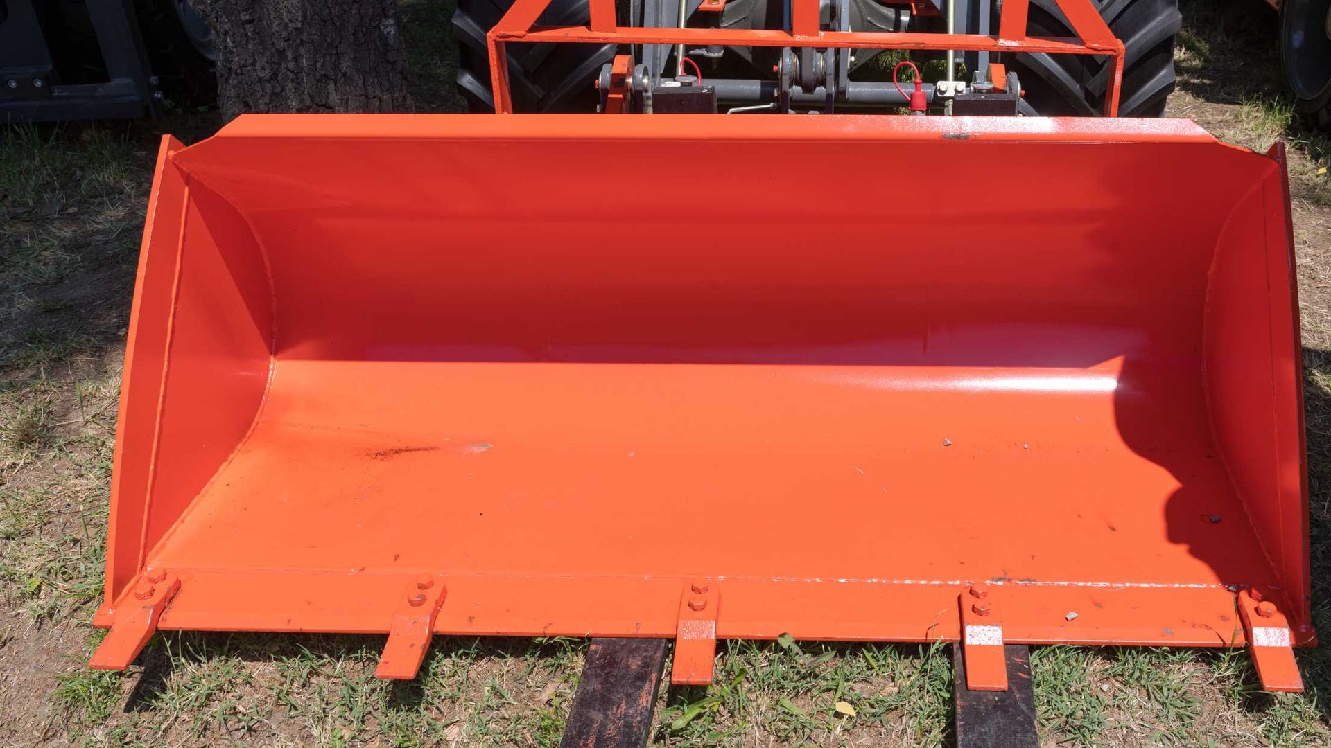An orange bucket is sitting on the grass next to a tractor.