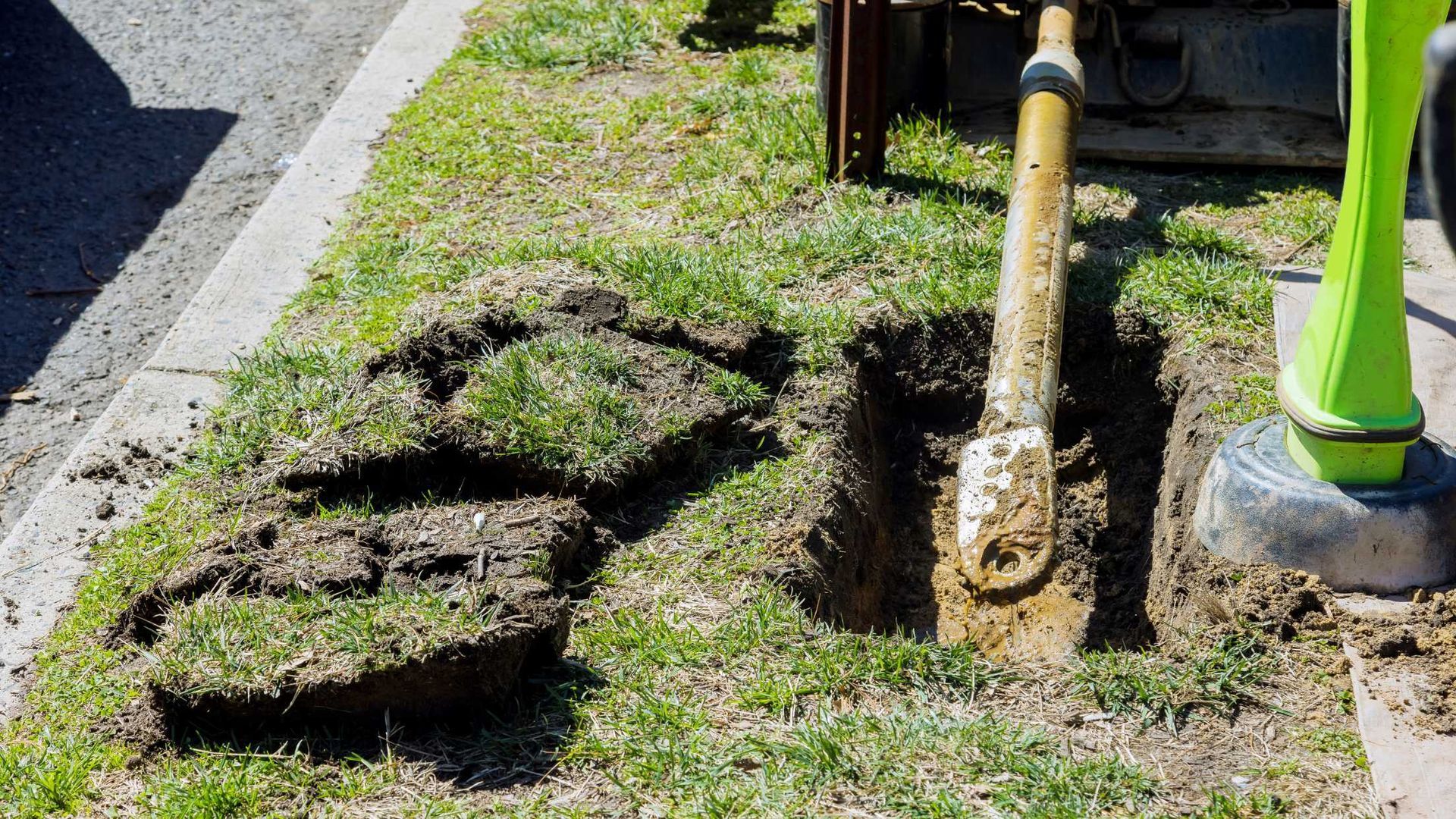 A shovel is digging a hole in the grass on the side of the road.