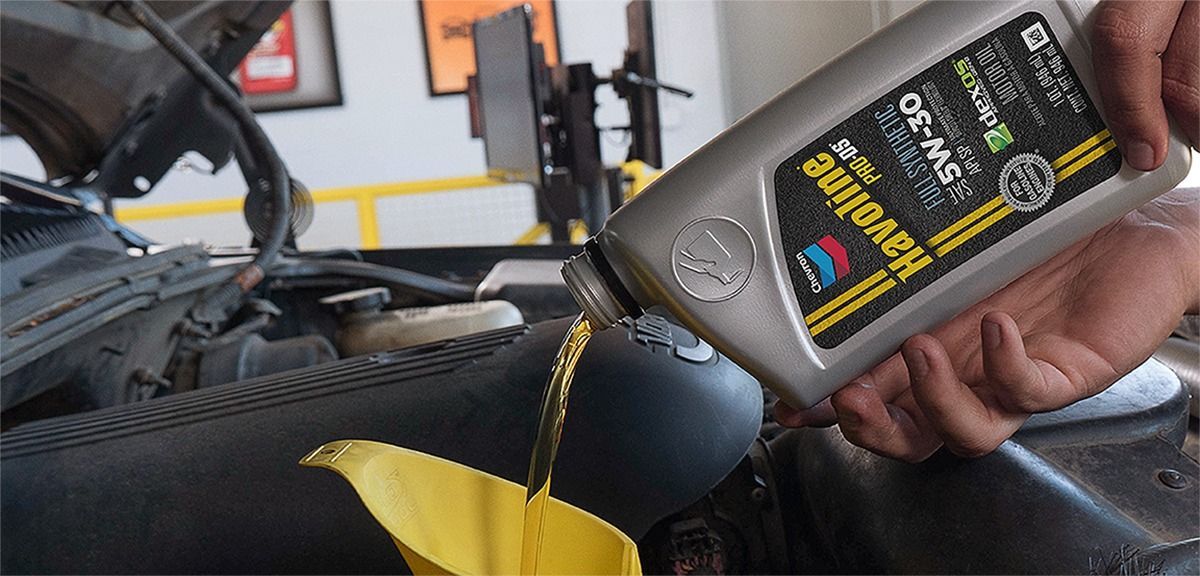 A person pouring oil from a Valvoline 5W-30 bottle into a funnel in a car engine.