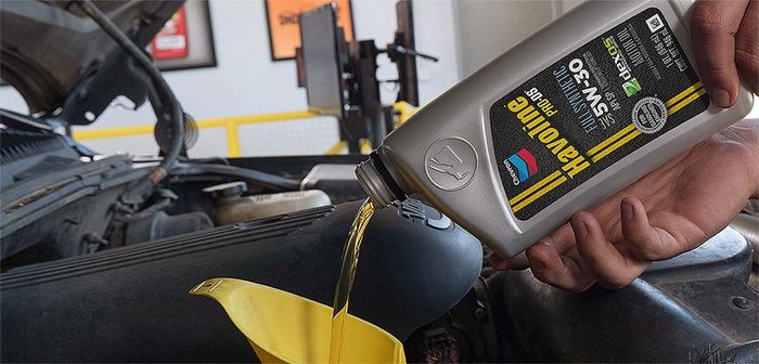 A person pouring oil from a Valvoline 5W-30 bottle into a funnel in a car engine.