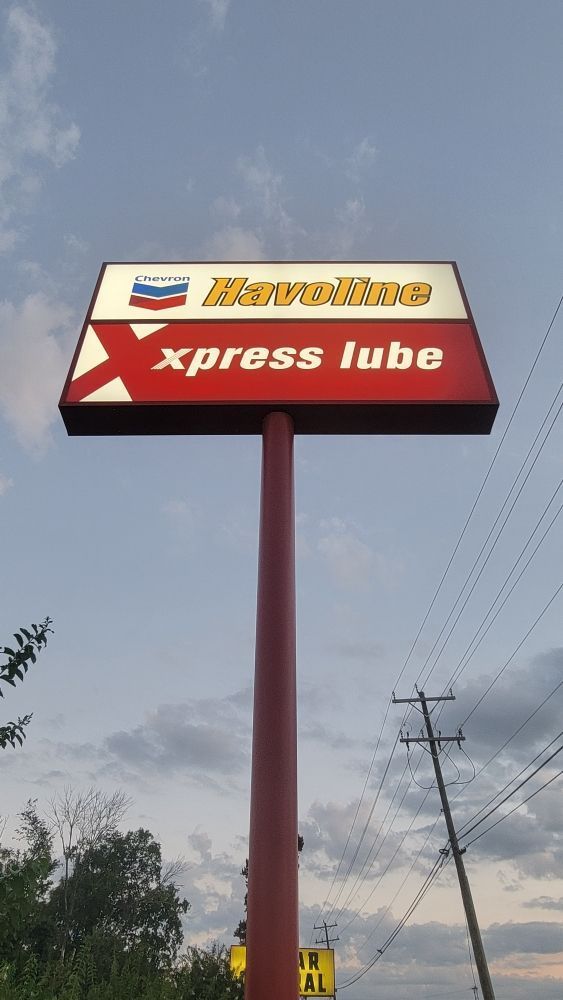 Sign for Chevron gas station and Xpress Lube, red and white, against a cloudy sky.