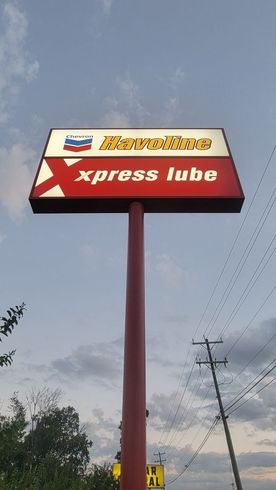 Sign for Chevron gas station and Xpress Lube, red and white, against a cloudy sky.