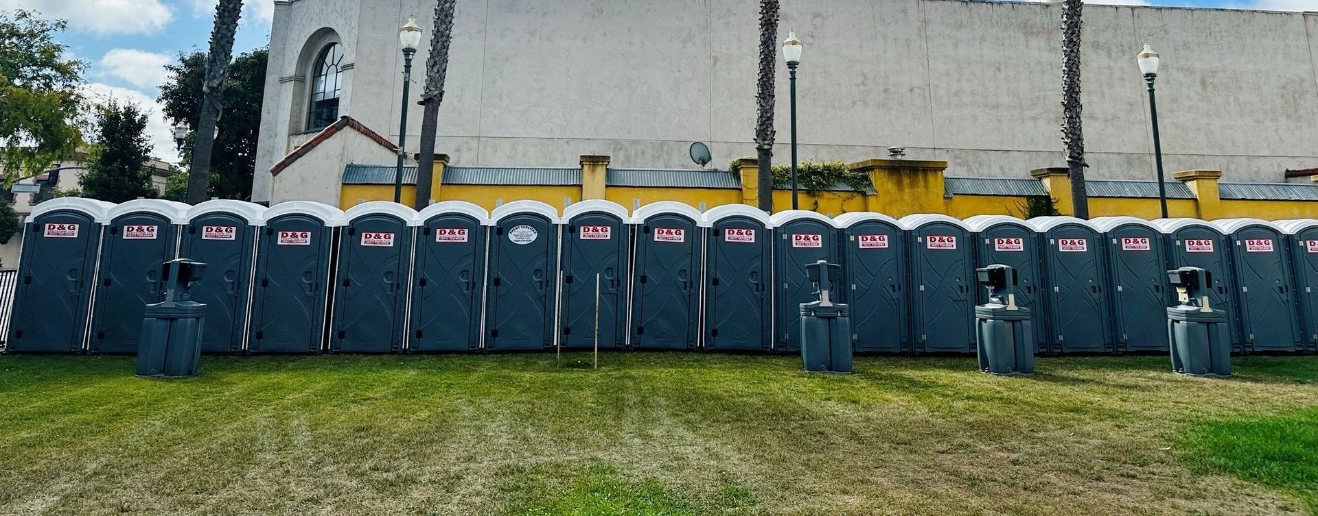 A row of blue portable toilets are lined up in front of a stone wall.
