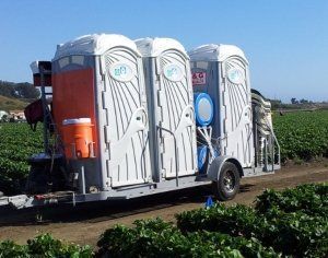 A trailer with three portable toilets on it is parked in a field.