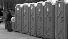 A man is standing in front of a row of portable toilets.