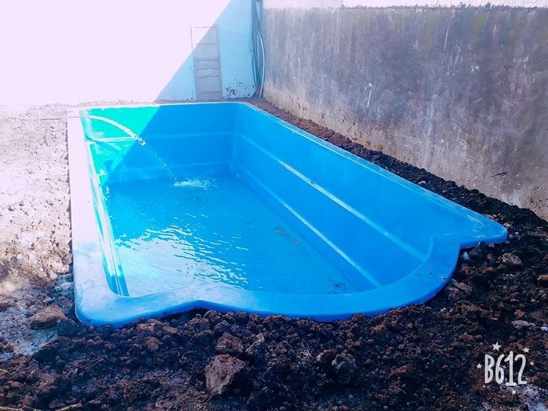 Piscina de fibra de vidrio de color azul, parcialmente llena de agua, empotrada en tierra.