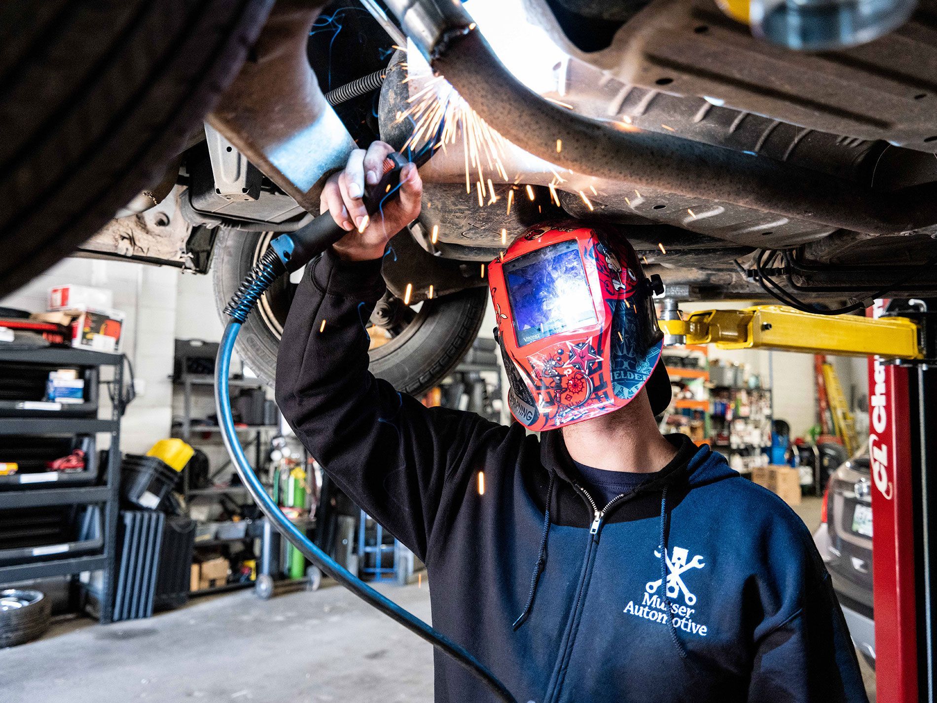 A certified technician wearing a welding mask repairing  a car exhaust pipe at Musser Automotive in bowling green kentucky