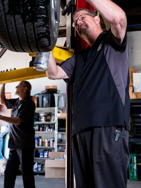 Service manager Dwayne checking a tire for leaks on a lift, with senior technician assisting at Musser Automotive.